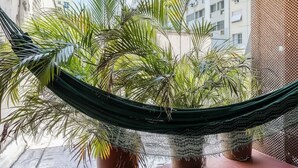 Eine Hängematze, die zwischen zwei Blumentöpfen auf einem Balkon gespannt ist, mit Blick auf Wohnhäuser.