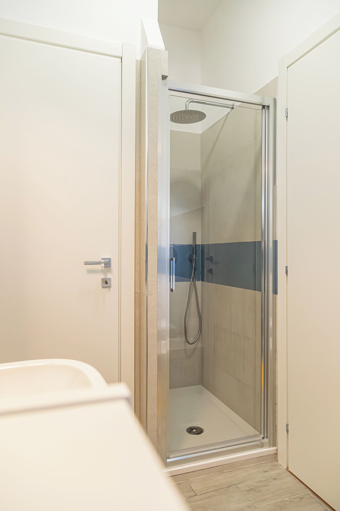 A glass-enclosed shower with a showerhead, a door handle, and a small drain.