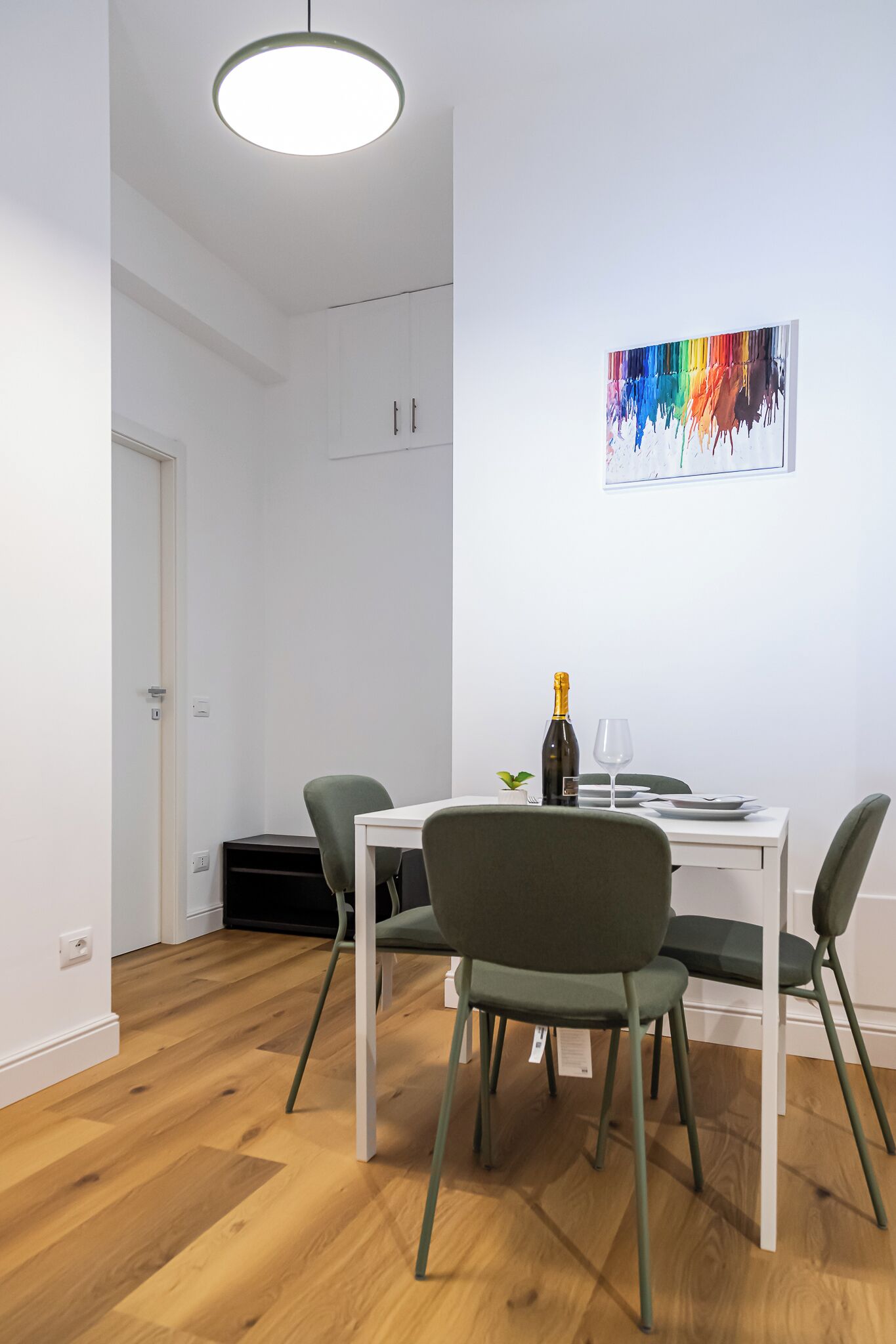 A dining area with a table, chairs, a bottle of champagne, and a painting on the wall.