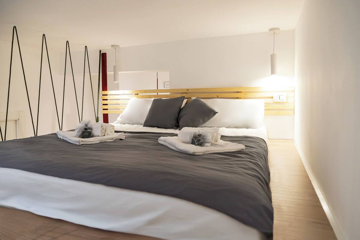 Une chambre d’hôtel moderne avec un lit bien fait, une tête de lit en bois et une table de chevet avec une lampe.
