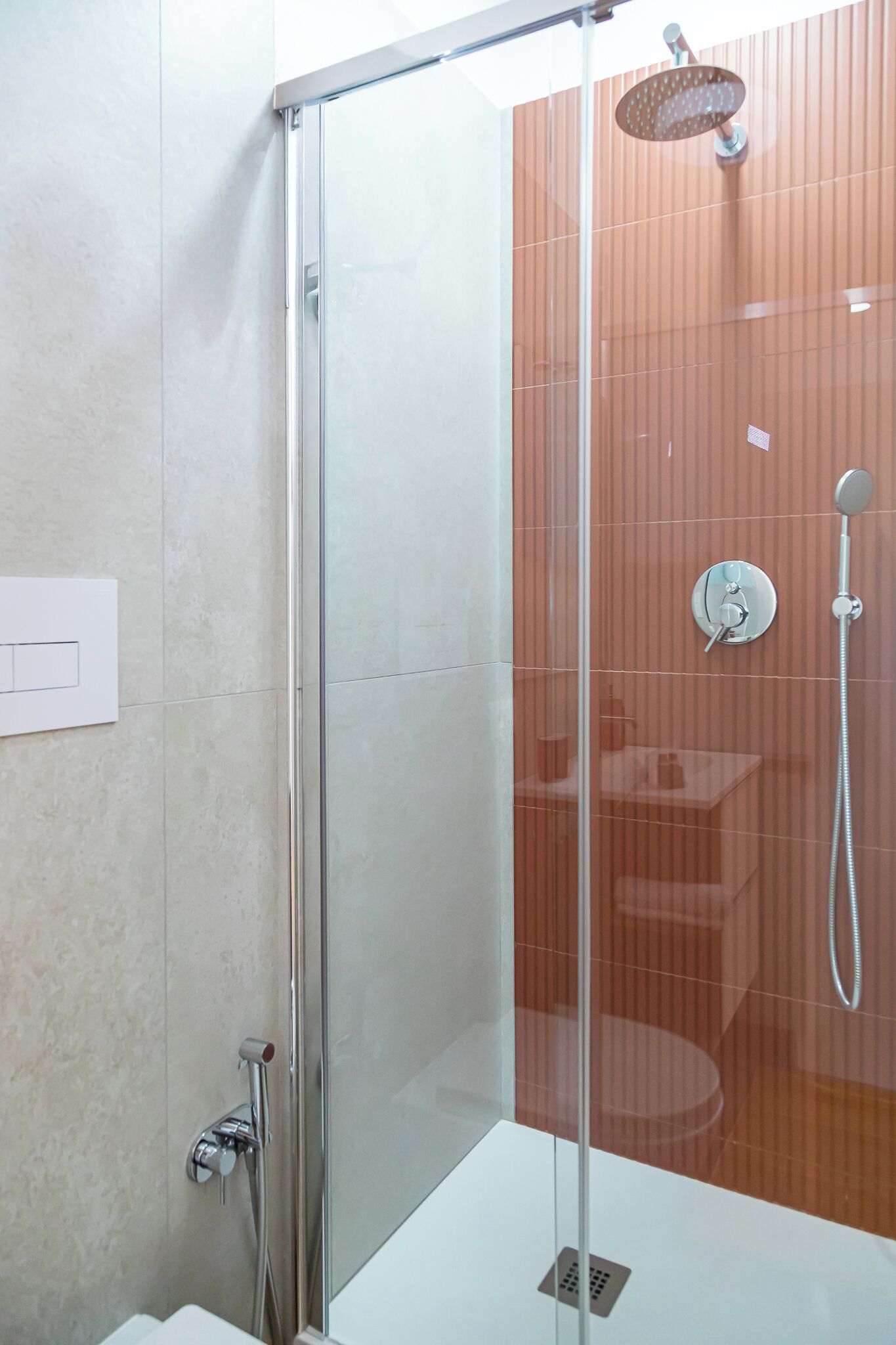 A modern bathroom with a glass shower enclosure, a white sink, and a wall-mounted faucet.