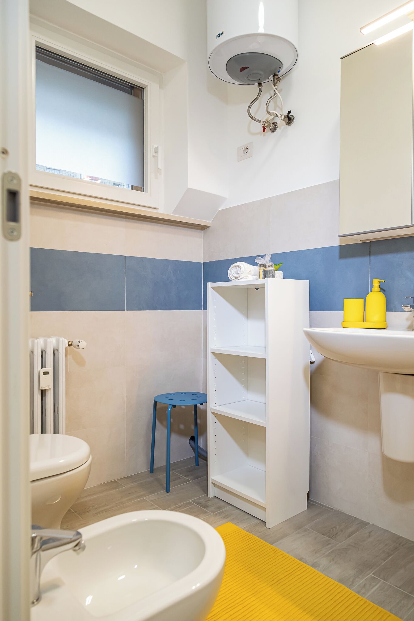 A bathroom with a toilet, bidet, sink, and a window.