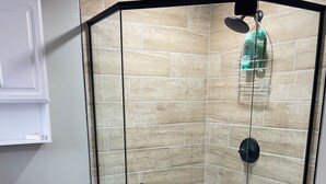 A modern bathroom with a glass-enclosed shower, a white toilet, and a blue trash bin.