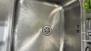 A stainless steel kitchen sink with a drain, a soap dispenser, and a dish rack.