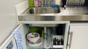 A compact kitchen with a stainless steel sink, a dish rack, and various kitchen utensils.