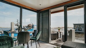 Un intérieur moderne avec vue sur la mer, comprenant un coin repas avec des chaises et une table, ainsi qu’un coin salon avec un canapé et une plante en pot.