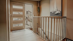 Ein Flur mit einer Holztreppe, einer beigen Tür mit Glasfeldern und einem gerahmten Bild von Segelbooten an der Wand.
