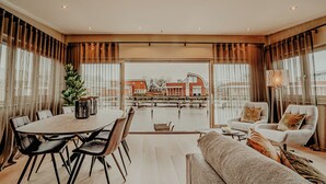 Ein geräumiger Wohnbereich mit Esstisch und Stühlen, einer Couch und Blick auf ein Gewässer sowie Gebäude im Hintergrund.