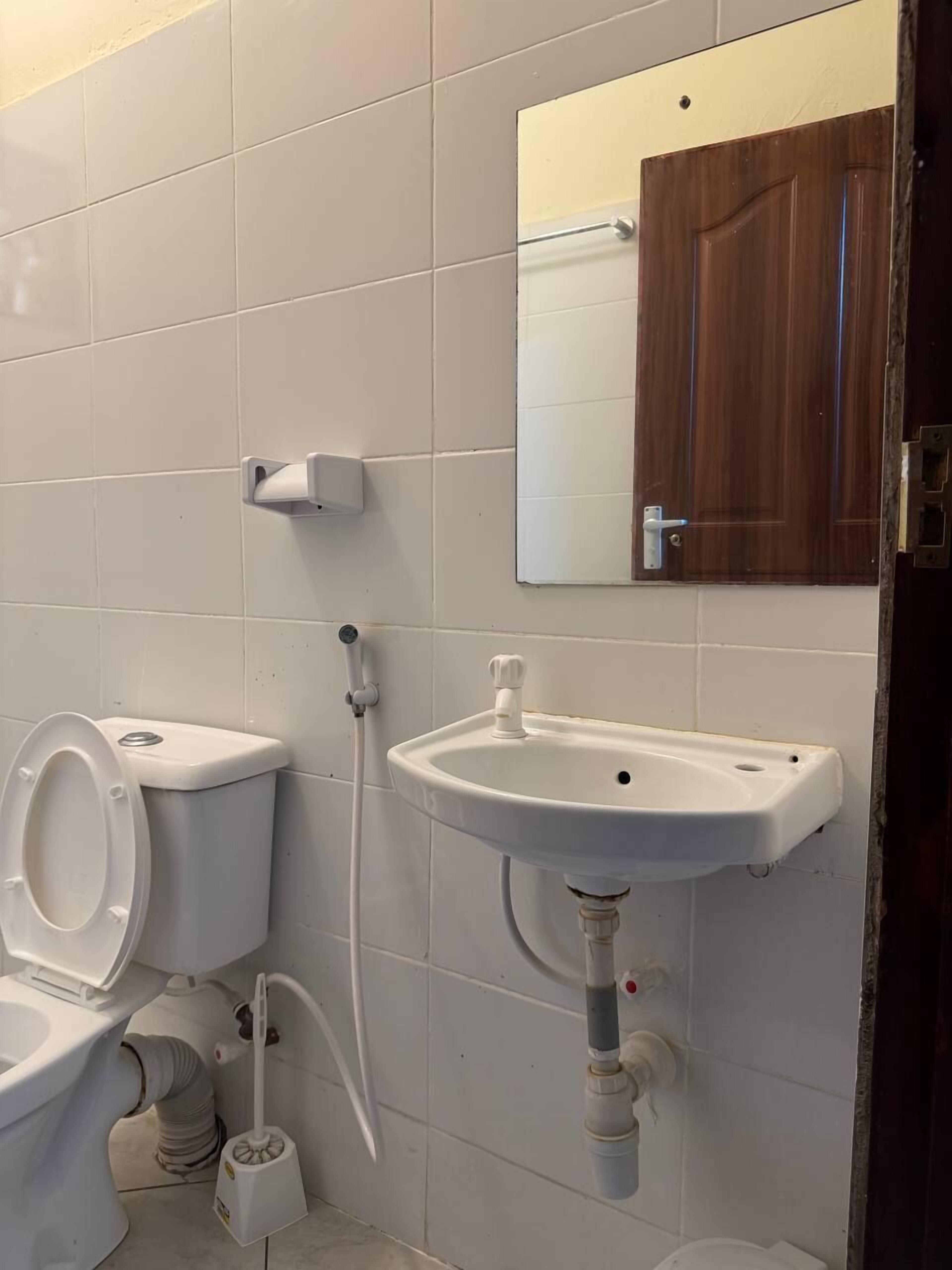 A bathroom with a toilet, a sink, a mirror, and a wooden door.