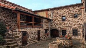 Edificio de piedra con patio, puertas de madera y un pequeño jardín con macetas.