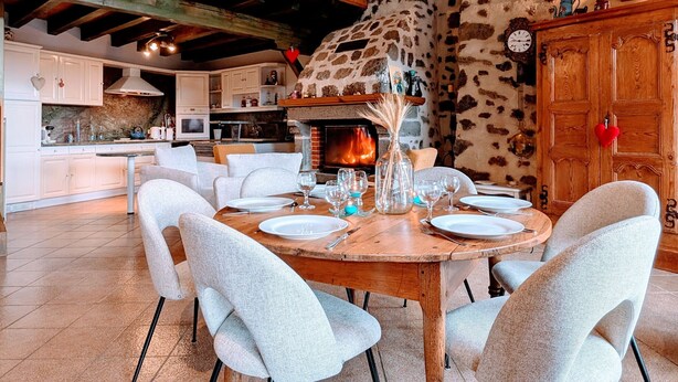 Un comedor con chimenea, sillas blancas y una mesa de madera dispuesta para cuatro.