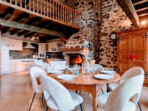 A dining area with a fireplace, white chairs, and a wooden table set for four. - Old farmhouse with stunning views - 4 guests (Polignac)