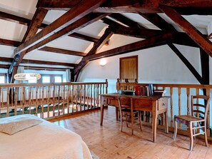 A room with exposed wooden beams, a wooden desk with books, a chair, and a bed with a patterned bedspread. - Old farmhouse with stunning views - 4 guests (Polignac)