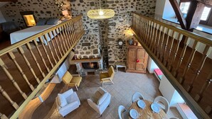 Un interior rústico con pared de piedra, escalera de madera, chimenea y zonas de estar.