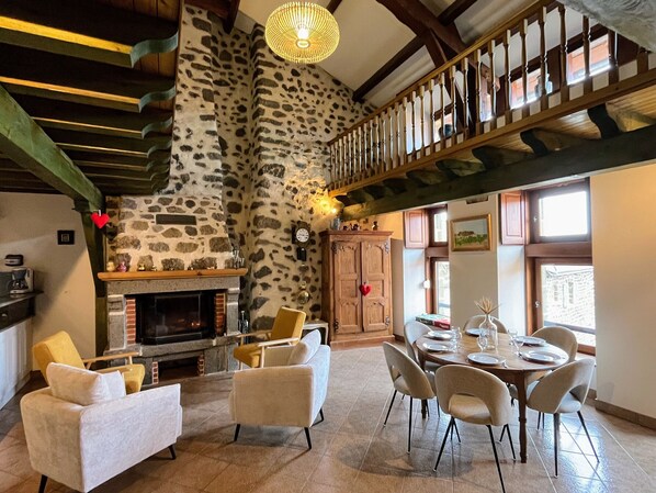 A spacious living area with a fireplace, stone wall, wooden staircase, dining table, and comfortable seating. - Old farmhouse with stunning views - 4 guests (Polignac)