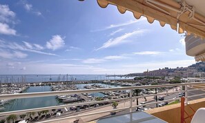 Un balcon offrant une vue sur un port de plaisance, un paysage urbain côtier et un ciel dégagé.