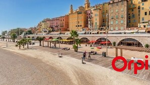 Un paseo marítimo con un puente de piedra, sombrillas de playa y un restaurante llamado 'Planet Sushi'.