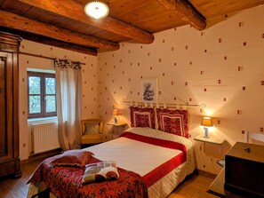 Une chambre avec un lit, deux tables de chevet avec des lampes, une fenêtre avec des rideaux, un radiateur et un plafond en bois.