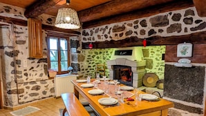 Ein rustikaler Essbereich mit Kamin aus Stein, Holztisch, Bänken und einer Pendelleuchte.