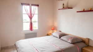Ein Schlafzimmer mit Bett, Nachttisch, Lampe, Fenster mit Vorhängen und einer Ablage mit Dekoration.