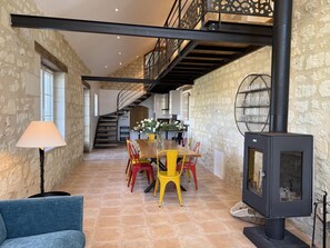 Une pièce spacieuse comprenant un coin repas, un escalier et un poêle à bois.