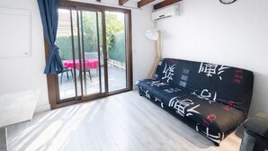 A room with a sliding glass door leading to an outdoor area, a sofa with patterned cushions, a clock on the wall, and an air conditioning unit. - Cozy house with AC and parking - 6 guests (Argelès-sur-Mer)