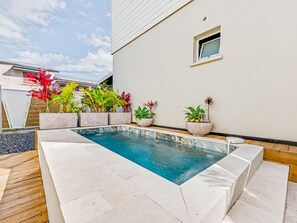 Ein Schwimmbecken mit Fliesenveranda, umgeben von Topfpflanzen, und ein kleines Fenster im angrenzenden Gebäude.