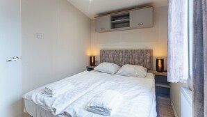 Ein ordentlich bezogenes Bett mit weißen Leinentüchern und Handtüchern, ein hölzerner Kopfteil, Nachttischlampen und ein eingebautes Regal über dem Bett.
