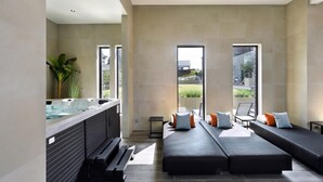 Un spa moderno con un jacuzzi, asientos con cojines y grandes ventanales que ofrecen vistas al exterior.