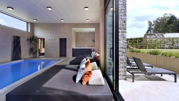 Un área interior de piscina moderna con zona de estar y pared de piedra.