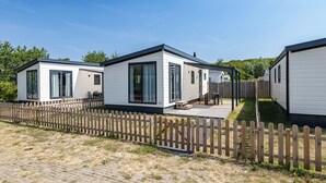 A row of mobile homes with a wooden fence in front, each with a patio area and large windows. - Duinhoeve chalet Schelp (Burgh-Haamstede)