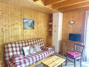 Ein gemütlicher Holzraum mit einem karierten Sofa, einem kleinen Holztisch, einem Fernseher und einem Sessel mit rosa Kissen.