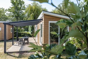 A wooden cabin with a covered patio and a table with chairs. - Duinhoeve Chalet Zeeland (huisdier toegestaan) (Burgh-Haamstede)