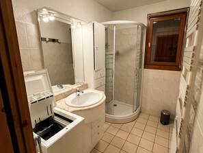Kylpyhuone, jossa on pesuallas, peili, suihku ja pieni roskakori.