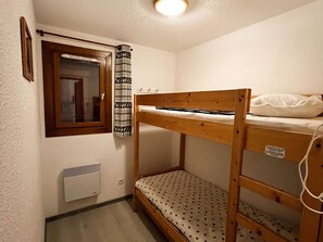 Pieni, kompakti huone, jossa on kerrossänky, ikkuna verholla, patteri ja seinään kiinnitetty lämmitin.
