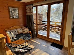 Une pièce chaleureuse avec un décor intérieur en bois, un canapé agrémenté de coussins à motifs, un fauteuil noir et de grandes fenêtres offrant une vue sur un paysage enneigé.
