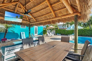 Un espacio exterior techado con piscina, sillones reclinables y una mesa.
