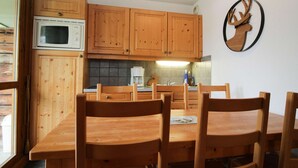 Een houten keuken met kastjes, een magnetron en een eettafel met stoelen.