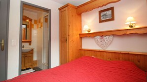 Een slaapkamer met een rood beddegoed, een houten garderobe en twee wandlampen.