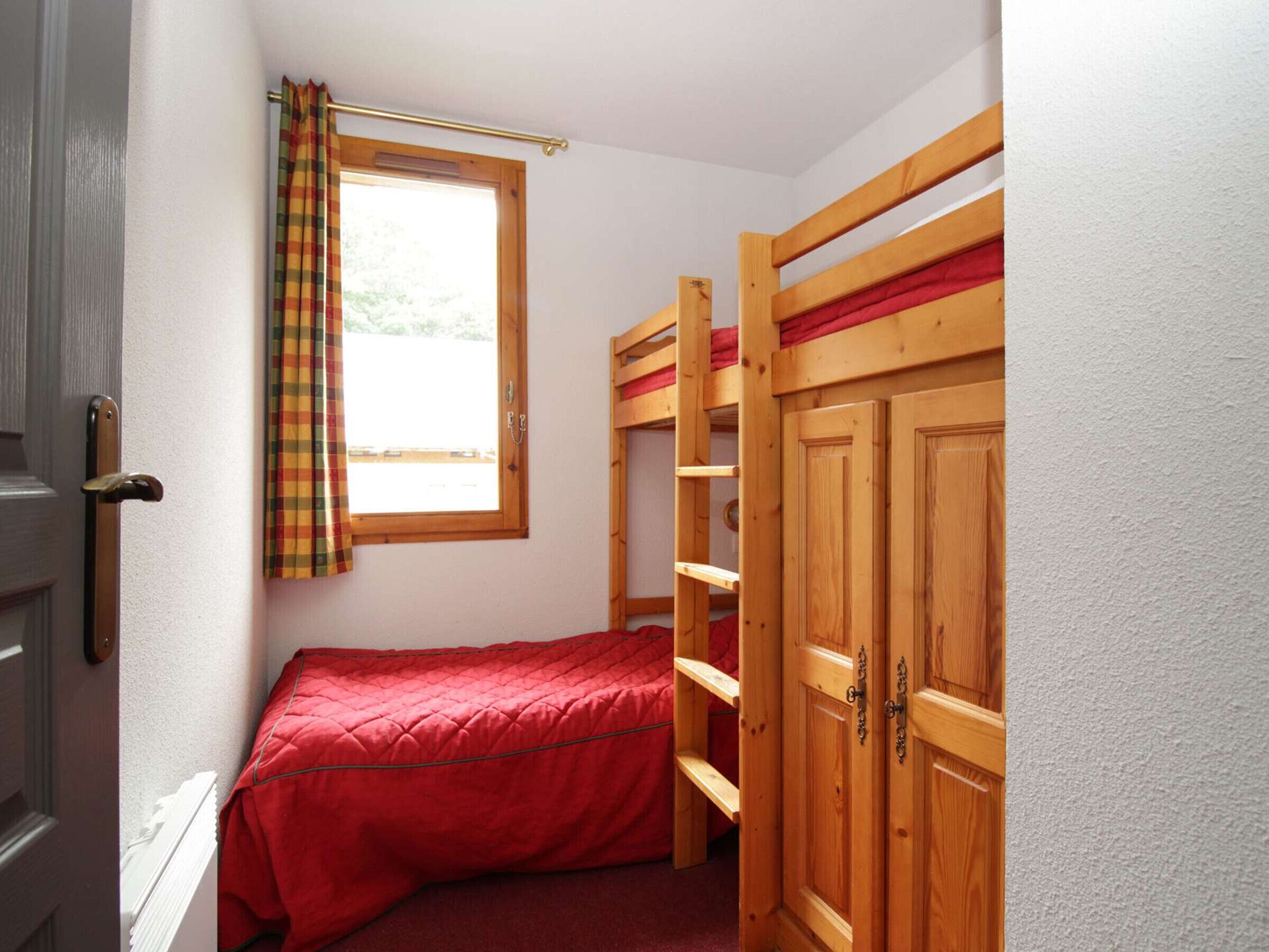 A small, cozy room with a bunk bed, a window with a curtain, and a door.