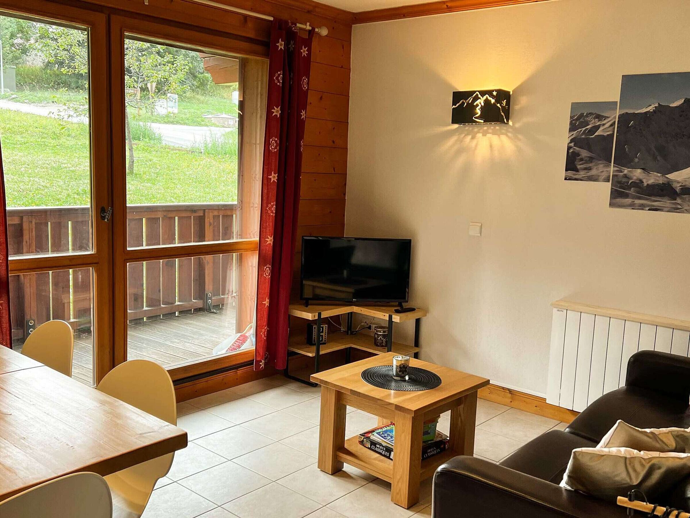 Un salon confortable avec un téléviseur, une table en bois, un canapé et une vue sur un jardin grâce à de grandes portes-fenêtres coulissantes.