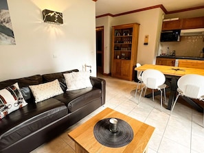 Un salon avec un canapé en cuir, une table basse en bois et un coin repas comprenant une table en bois et des chaises blanches.