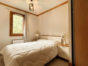 Une chambre à coucher comprenant un lit, une table de chevet, une lampe, une fenêtre avec des rideaux et un luminaire au plafond.