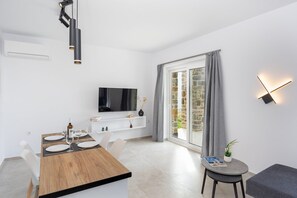 A modern dining area with a wooden table set for four, a flat-screen TV mounted on the wall, and a large window with curtains. - Naxos Cube Villa / Panoramic View Maisonette (Plaka)
