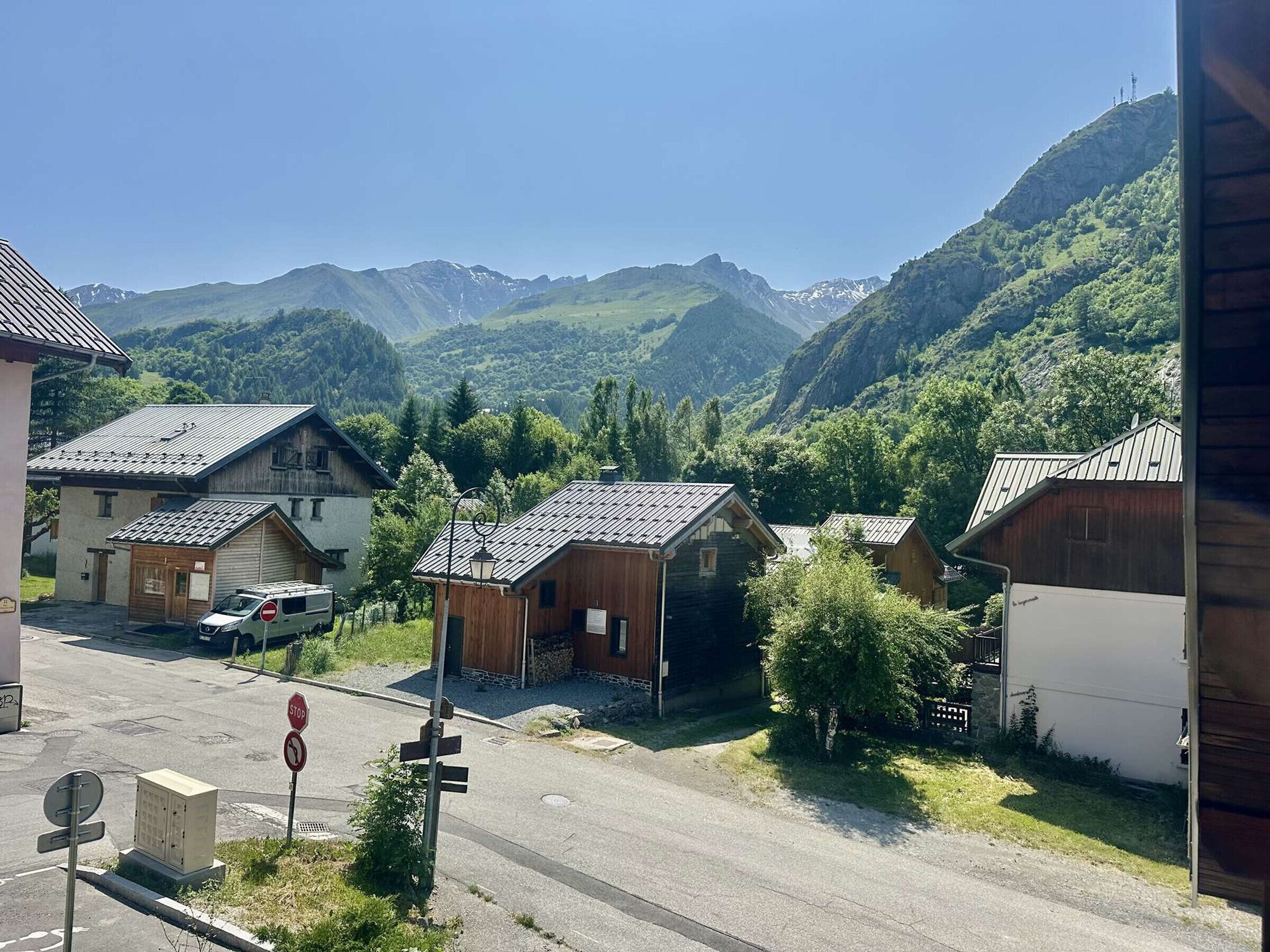 Un pueblo rural con casas de madera tradicionales, una señal de stop y montañas al fondo.