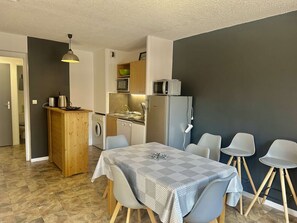A compact kitchen with a microwave, sink, and refrigerator, a dining area with a table and chairs, and a wooden cabinet. - Family apartment - 6 guests (Valloire)