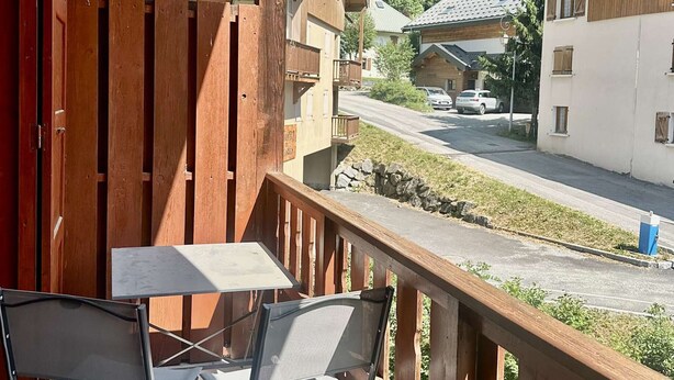 A wooden balcony with a table and chairs, overlooking a street with houses and a car. - Family apartment - 6 guests (Valloire)