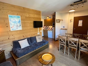 Une pièce confortable avec un canapé, une table à manger et des chaises, un coin cuisine et une affiche accrochée au mur.