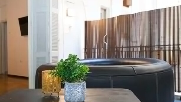 A modern interior with a black leather sofa, a small table with two decorative vases, and a wooden partition. - Athens Central Jacuzzi Retreat (Athens)