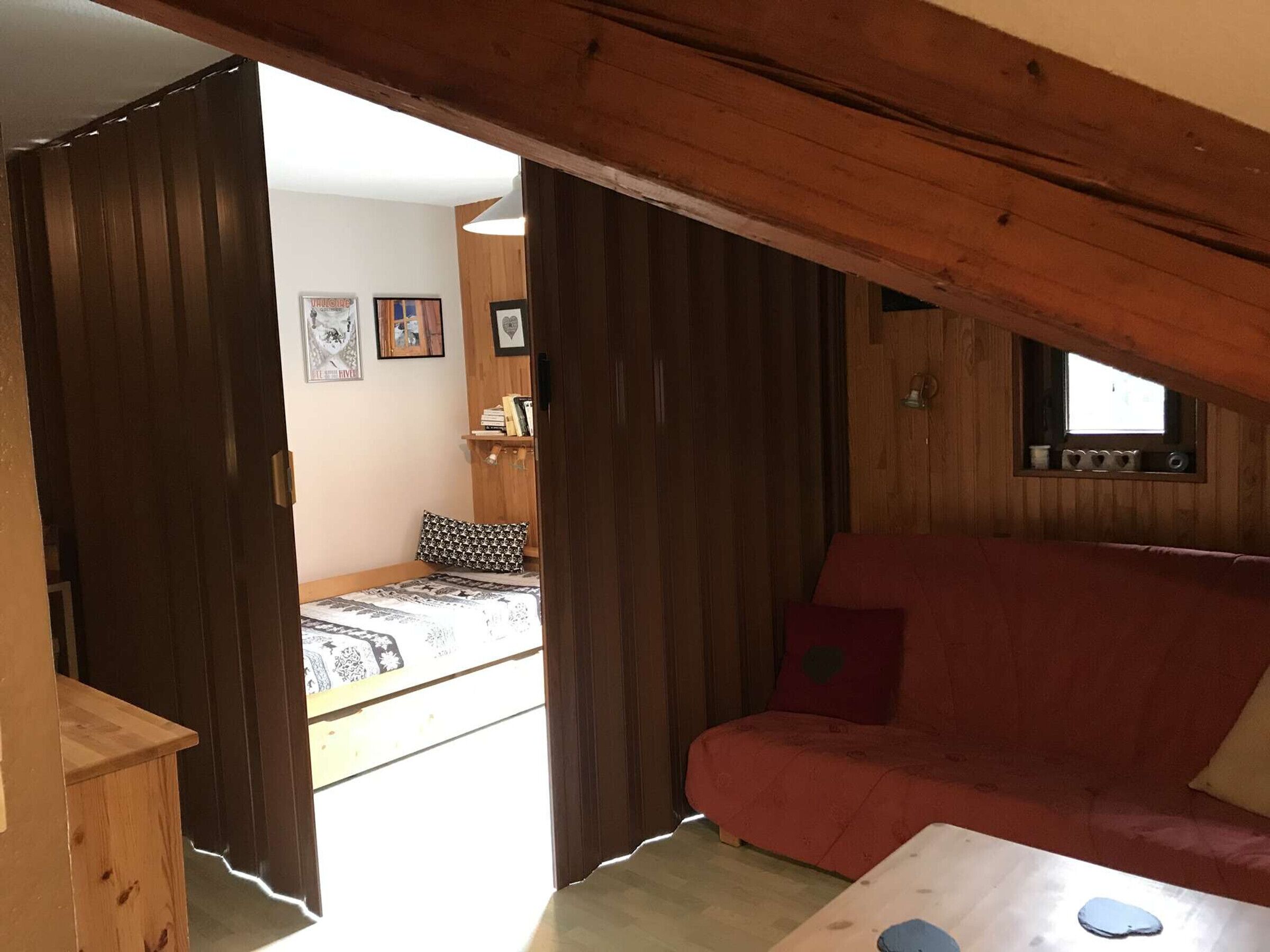 Una habitación acogedora con techo de madera, un sofá rojo, una cama con ropa de cama estampada y una ventana pequeña.